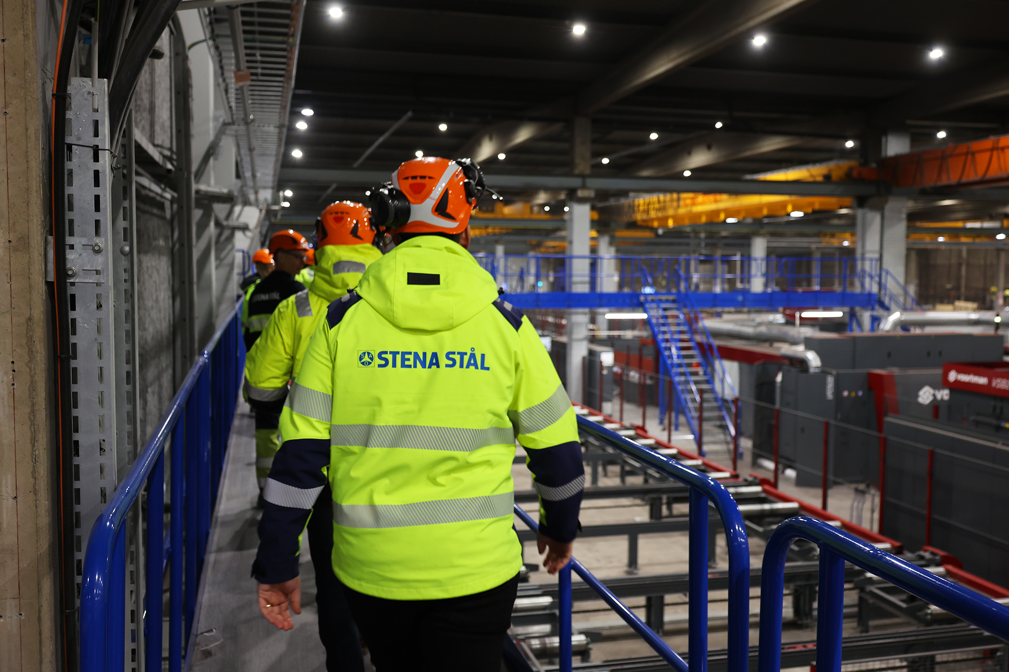 Människor i gula jackor och hjälmar går i en produktionsanläggning